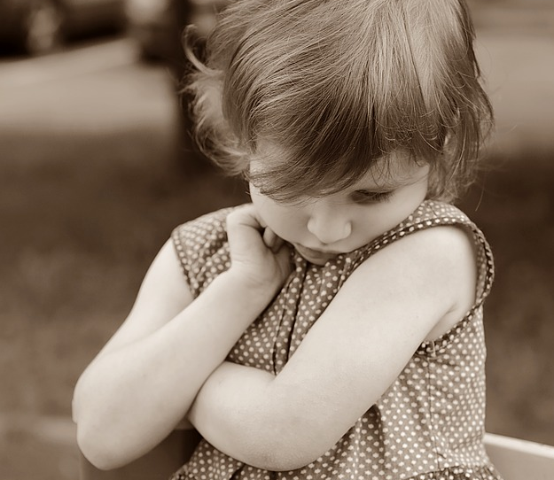A little girl in a polka dot dress is sitting with her arms crossed